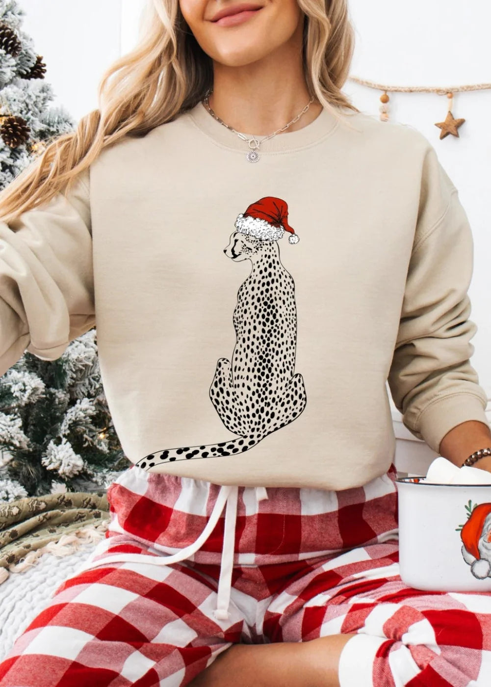 Person wearing a beige sweatshirt with a Christmas-themed design, sitting by a snowy outdoor scene.