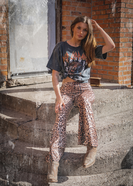 Woman wearing leopard print bell bottom pants with slim fit and flare leg
and Def Leppard graphic tee