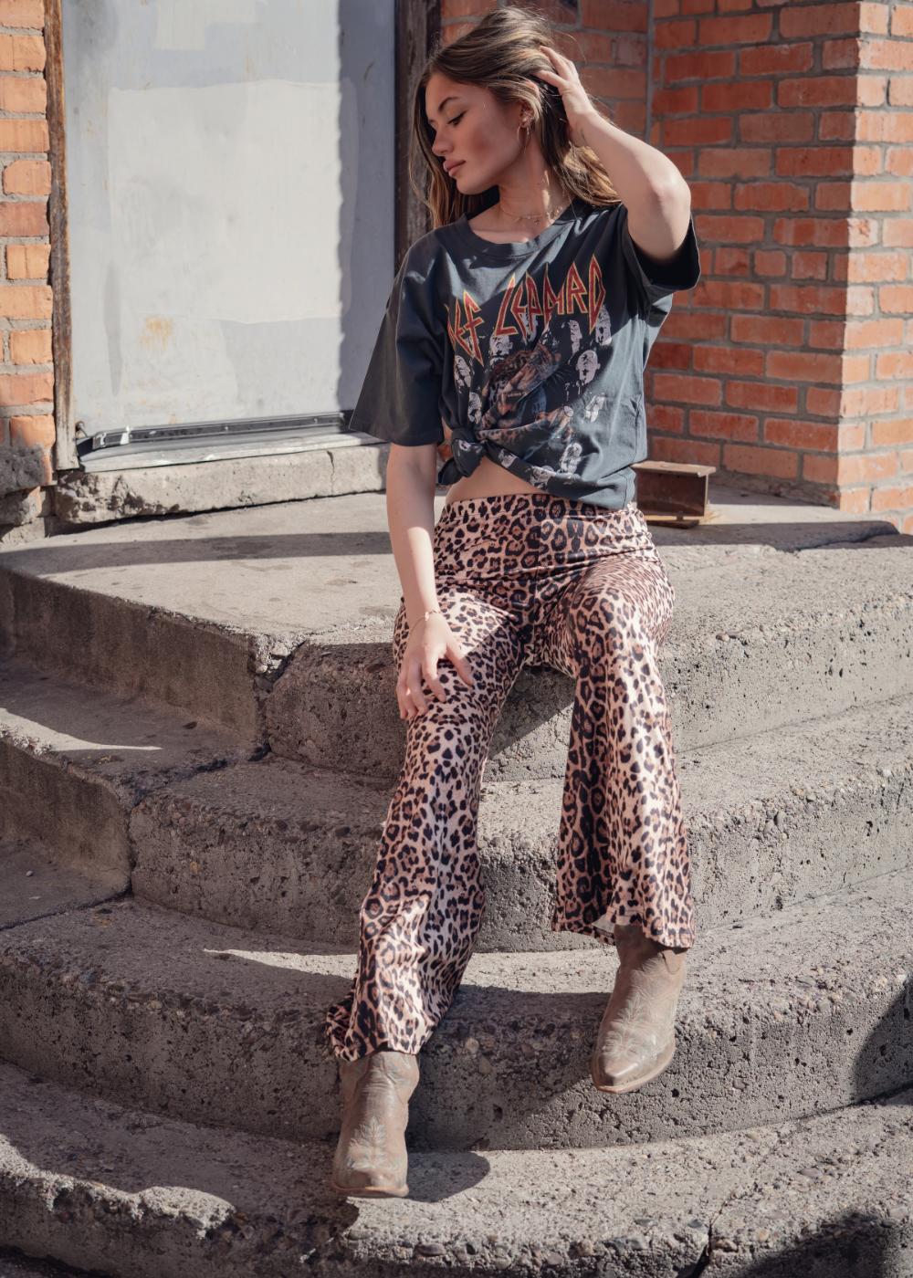Woman sitting on concrete steps wearing a graphic t-shirt and leopard print pants.