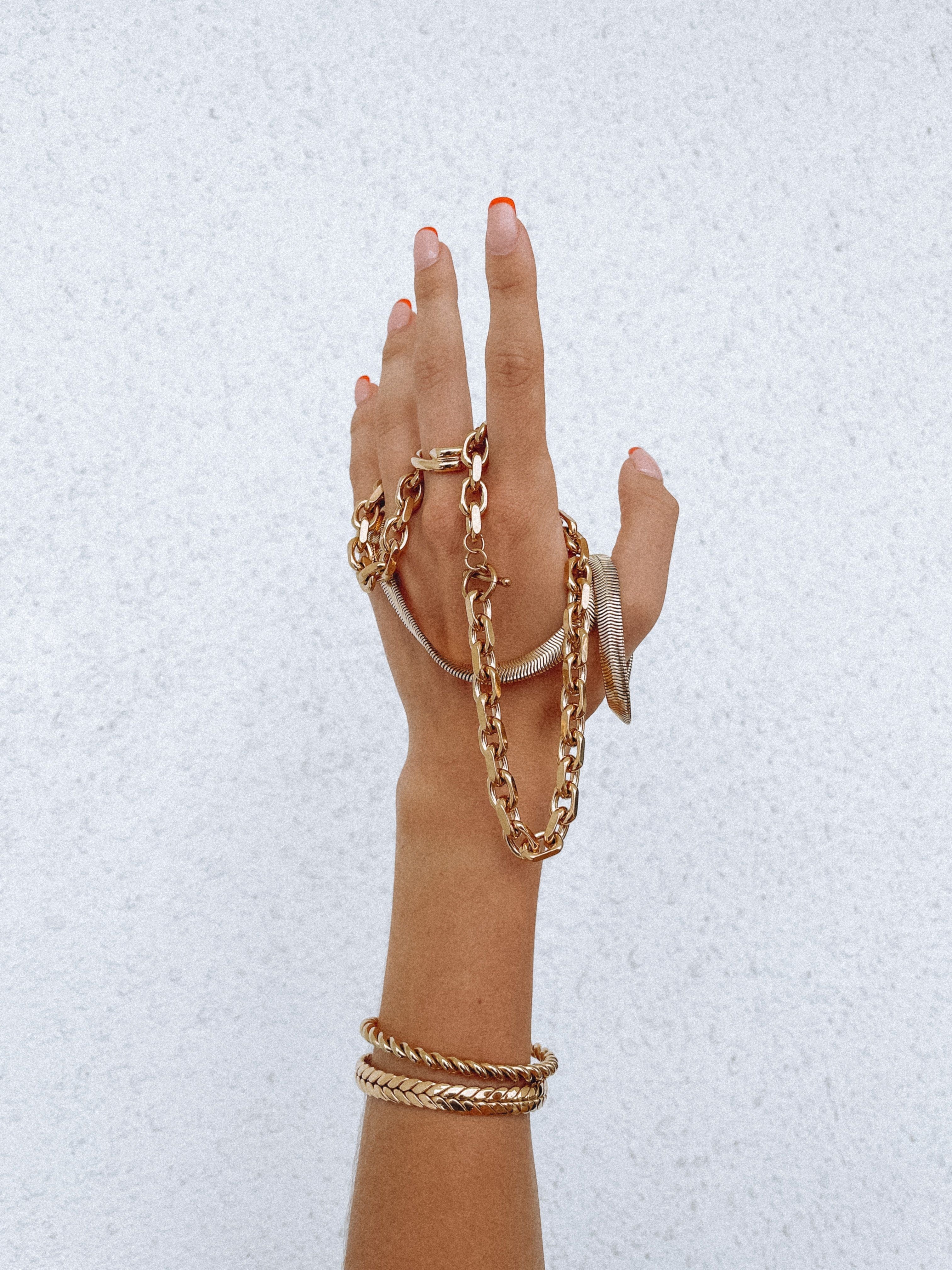 A womens hand holding gold bracelets and wearing 2 gold bracelets