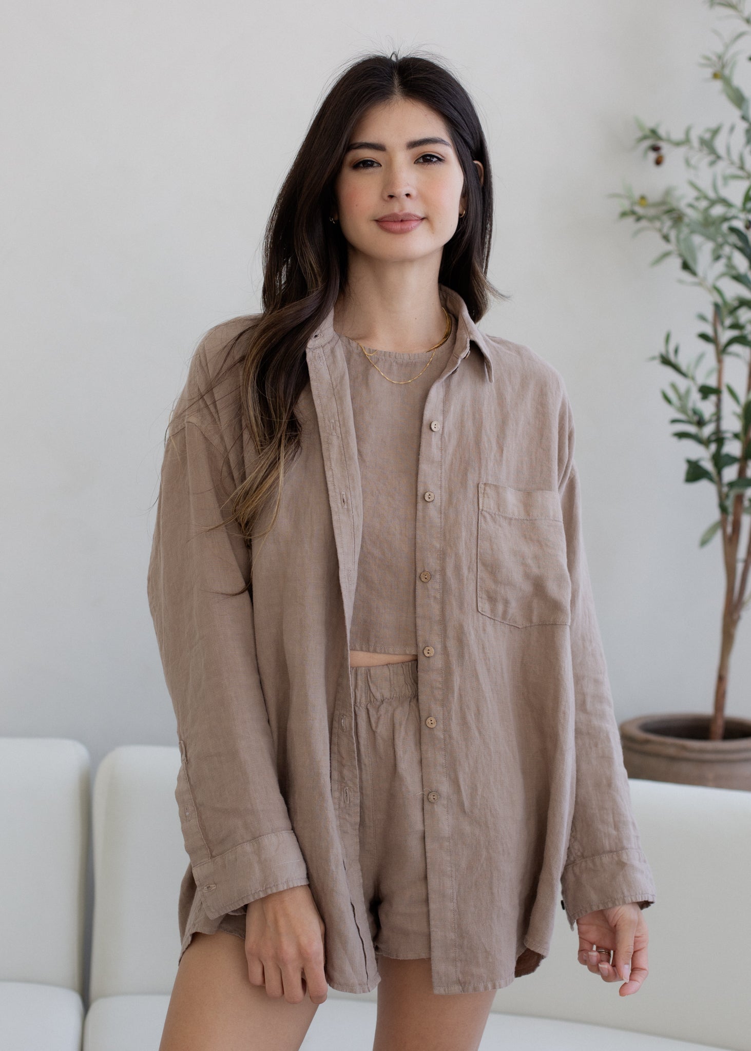 Woman wearing a beige shirt dress standing in a room with a white couch and plant.