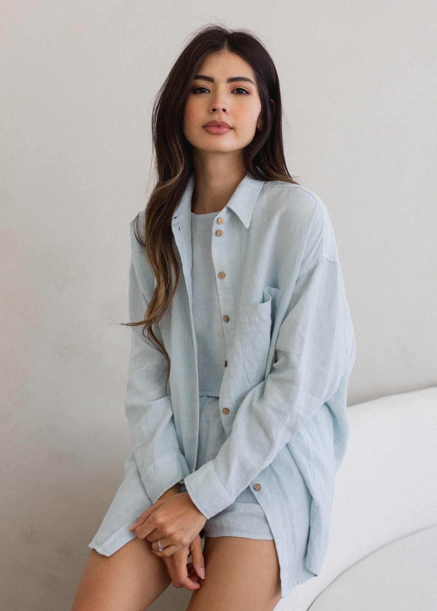 Woman wearing a light blue shirt and shorts sitting on a bed.