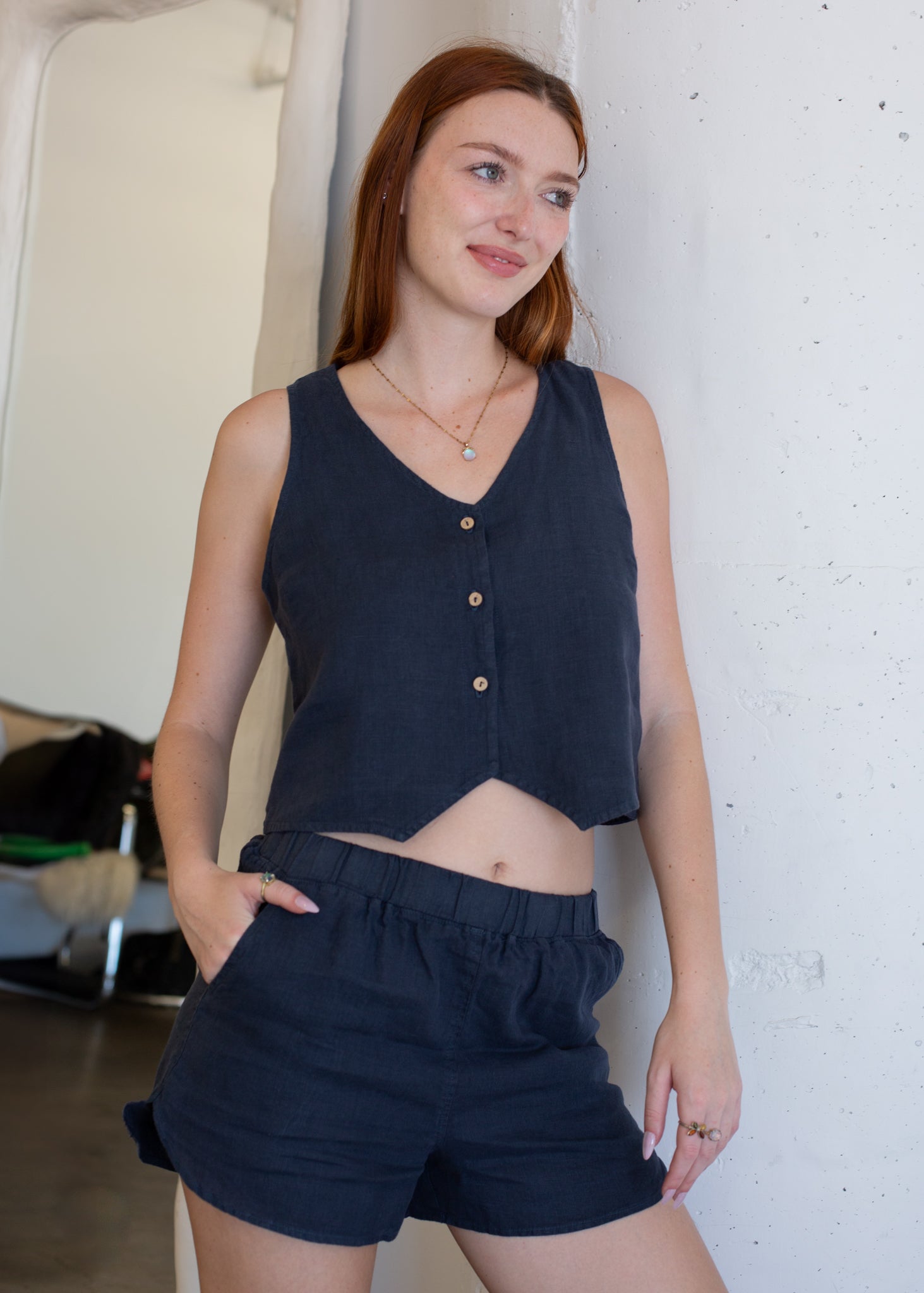 Woman wearing a navy sleeveless top and shorts against a white wall.
