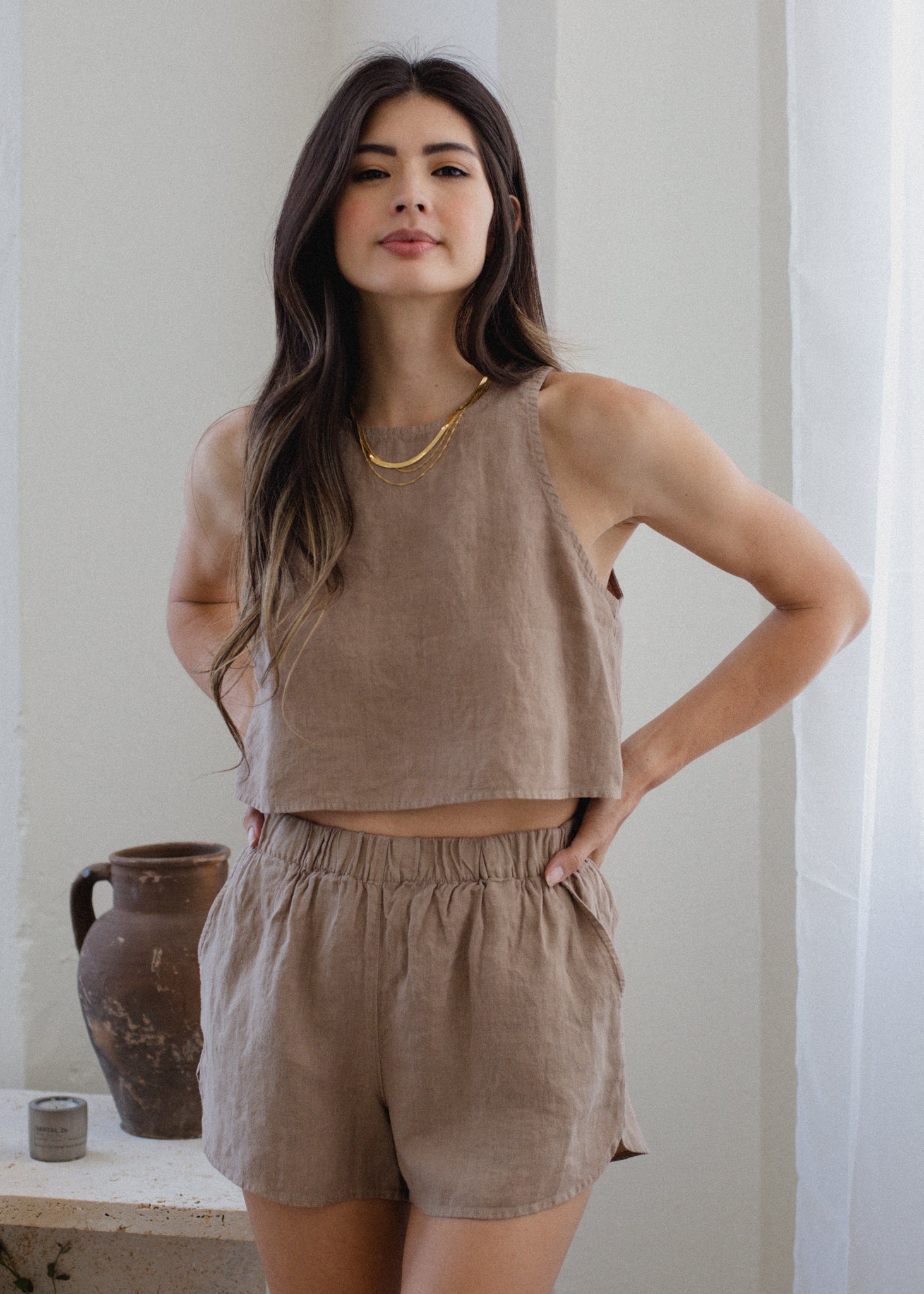 Woman wearing a brown sleeveless top and shorts standing against a neutral background.