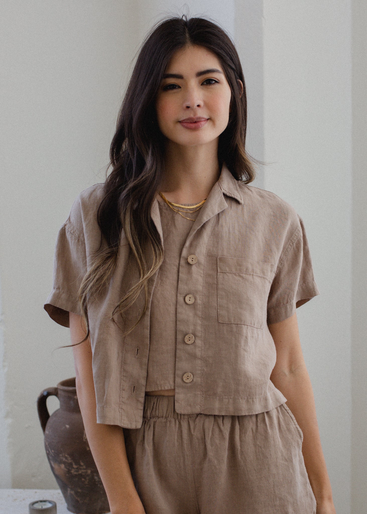 Woman wearing a beige linen outfit standing against a white wall.