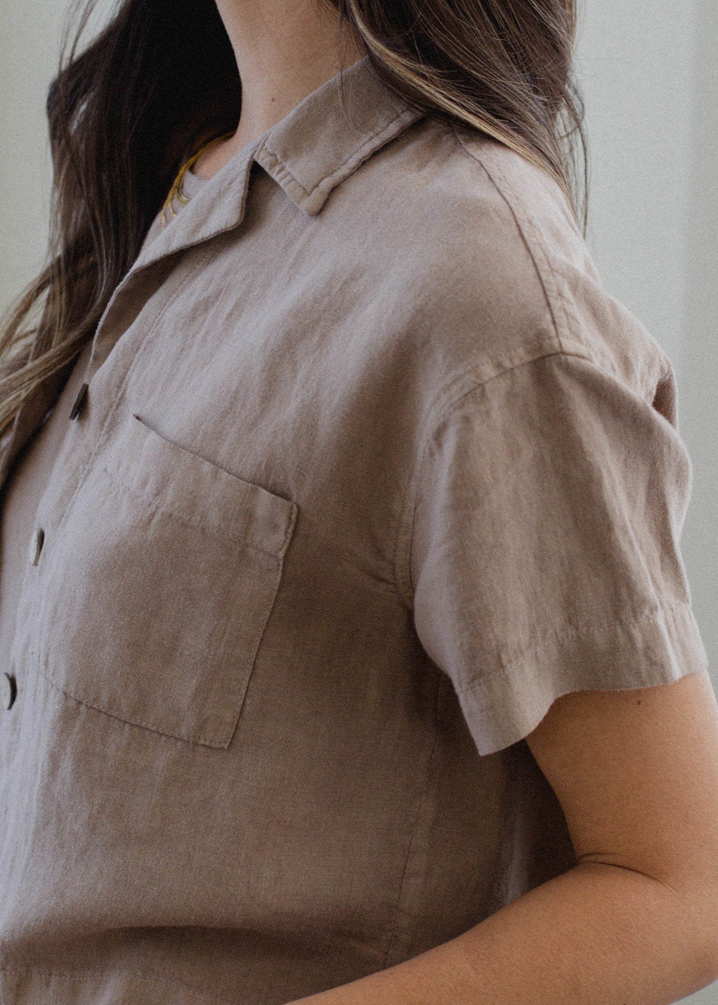 Person wearing a beige short-sleeve shirt with a neutral background