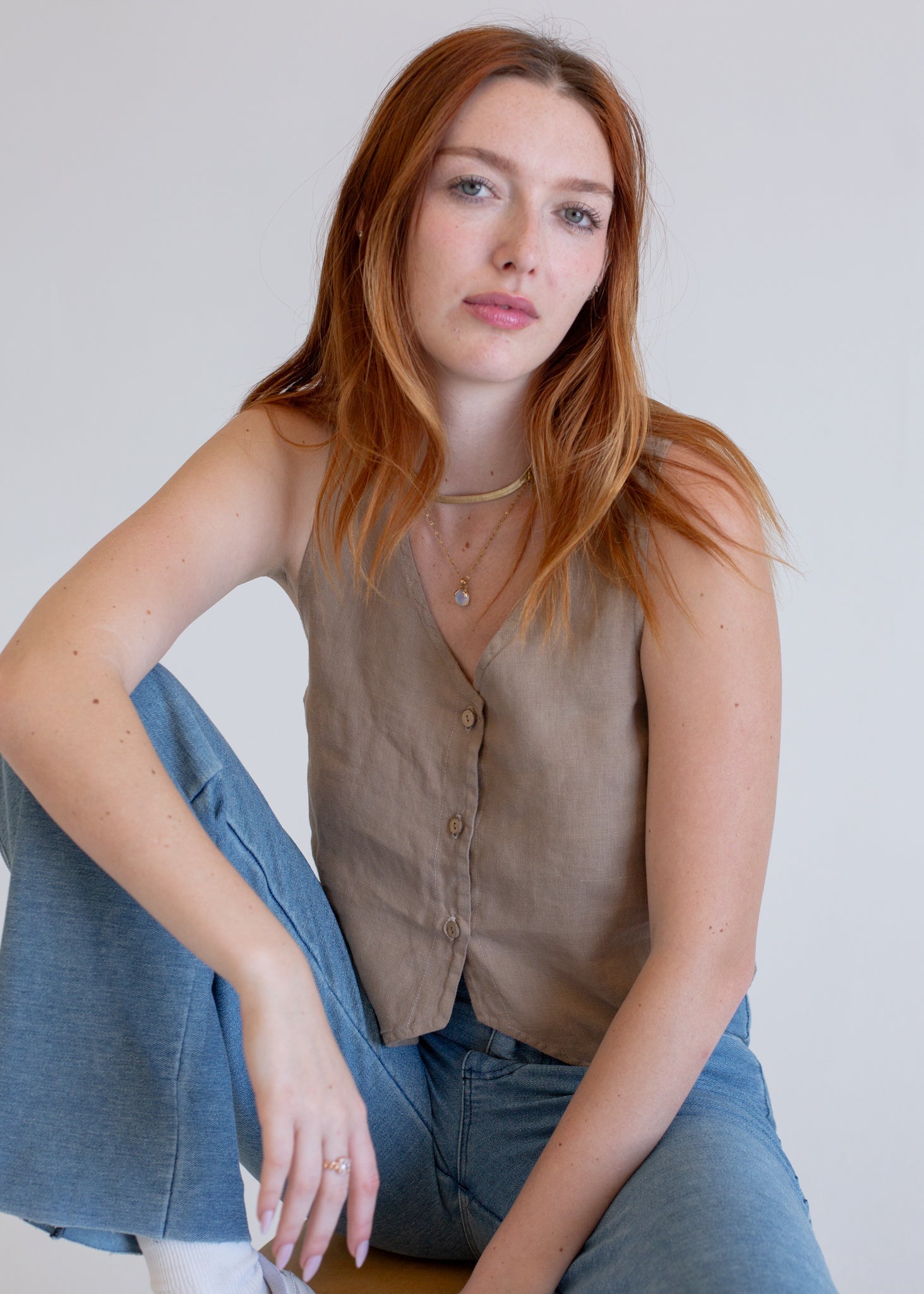 Woman wearing a brown vest and blue jeans against a plain background