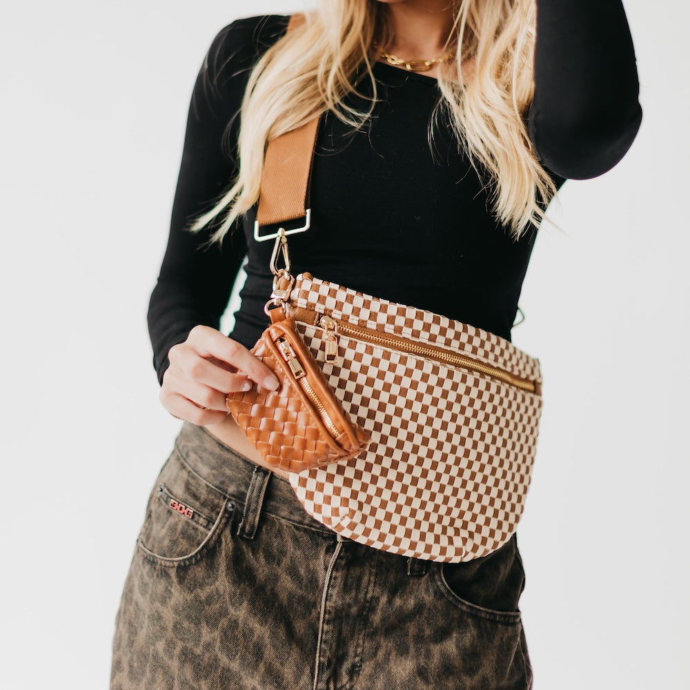 Person wearing a checkered waist bag with a mini brown wovenMini Westlyn Bag Charm – Clip-On Mini Bag Accessory for Cash, Cards & AirPods