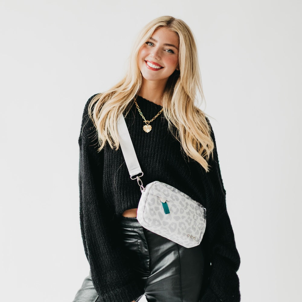 Woman wearing a black sweater and black pants with a white crossbody bag featuring a pattern.