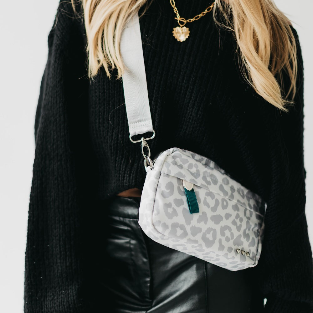 Person wearing a gray leopard print crossbody bag with a plain background