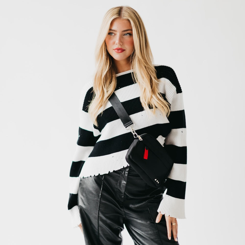 Woman wearing a black and white striped sweater with a black leather bag on a white background