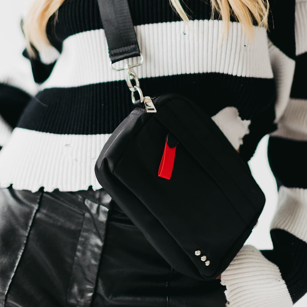 Black crossbody bag with a red tag held by a person wearing a black and white striped sweater.