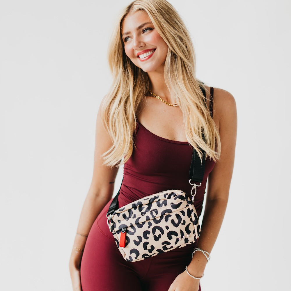Woman wearing a leopard print fanny pack on a plain background