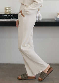 Person wearing white pants and brown sandals in a minimal indoor setting