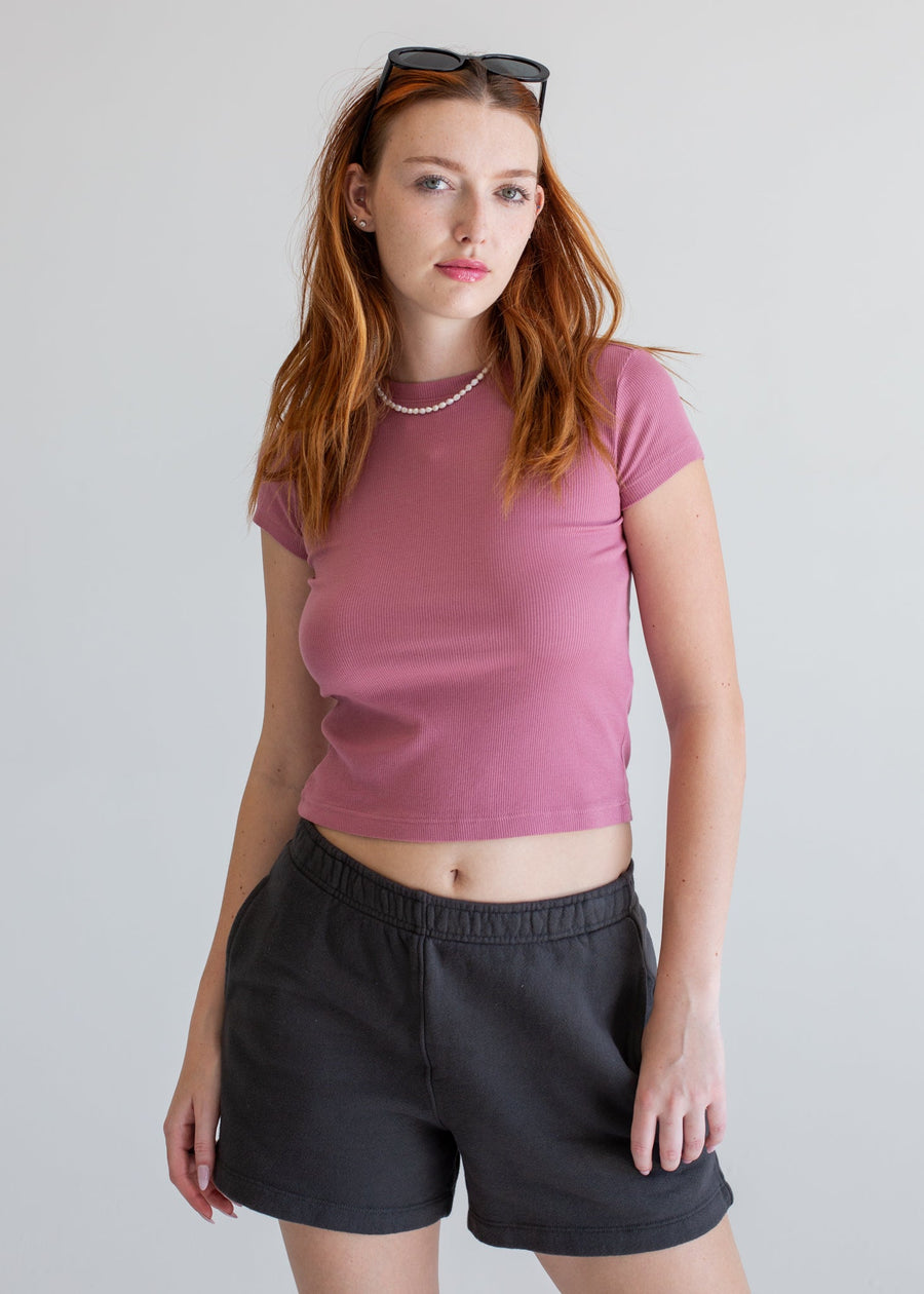Woman wearing a pink crop top and black shorts against a plain background