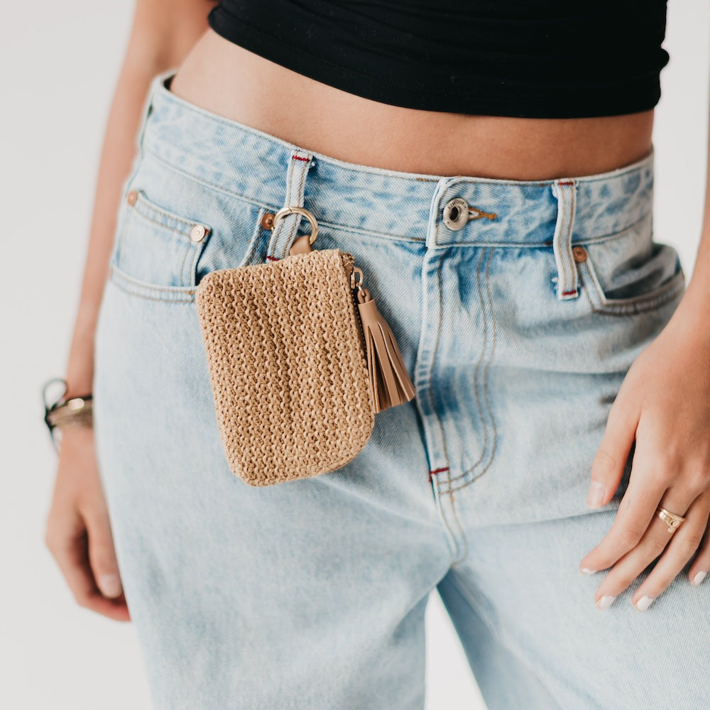 Person wearing light blue jeans with a woven pouch attached to the pocket.