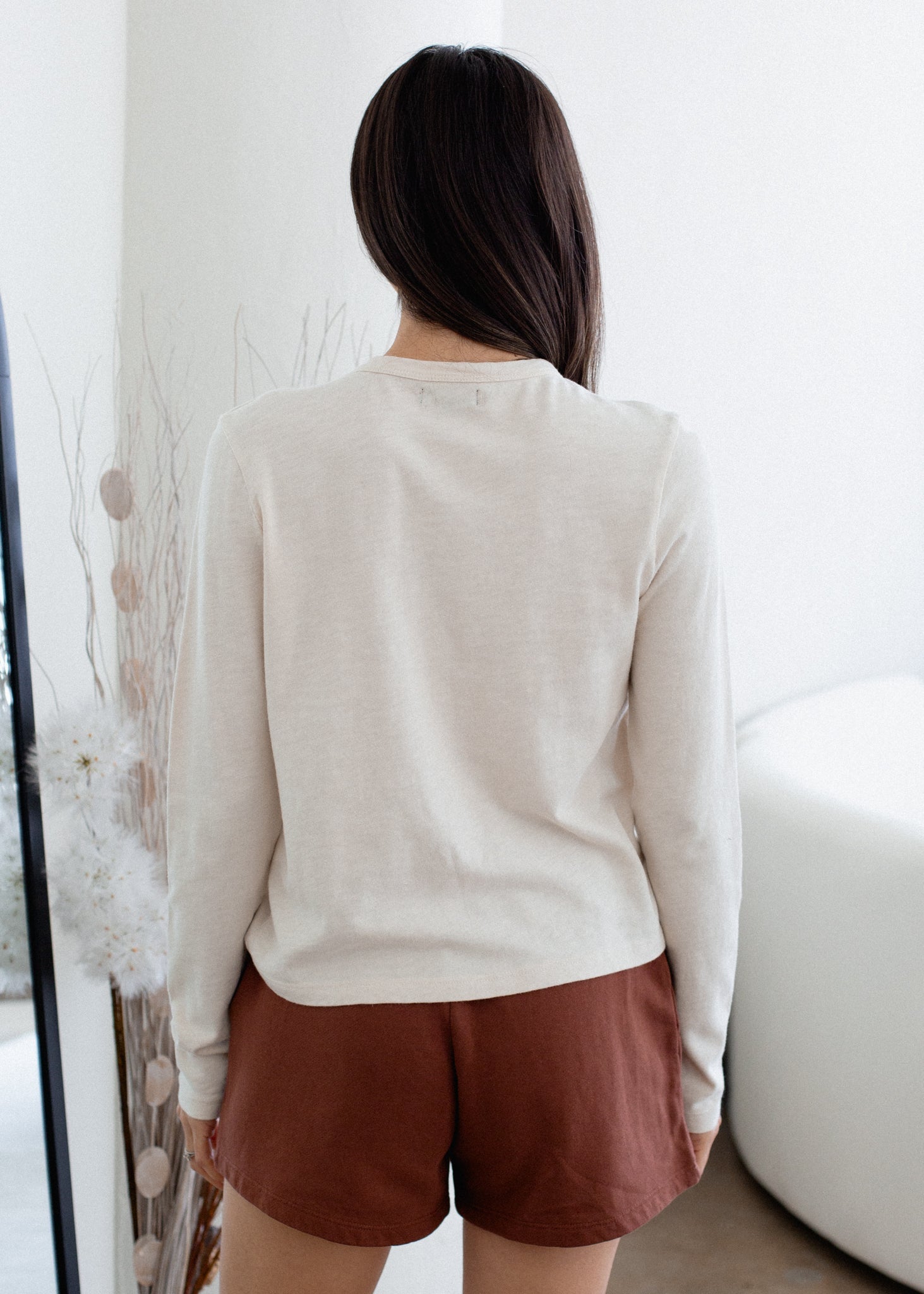 Person wearing a beige sweater and brown shorts in a minimal indoor setting