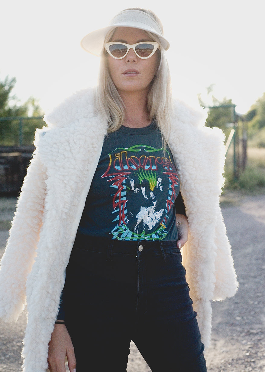 Person wearing a graphic t-shirt, white coat, and sunglasses outdoors.