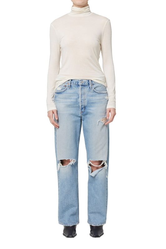 A model wearing the Agolde 90's Jean in "Threadbare," a pair of light indigo, mid-rise, straight-leg jeans with a destructed finish.