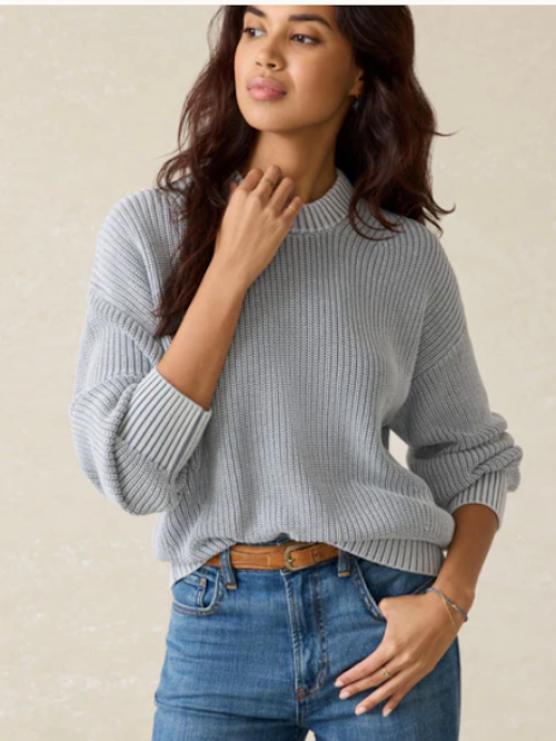 Woman wearing a gray sweater and blue jeans against a beige background
