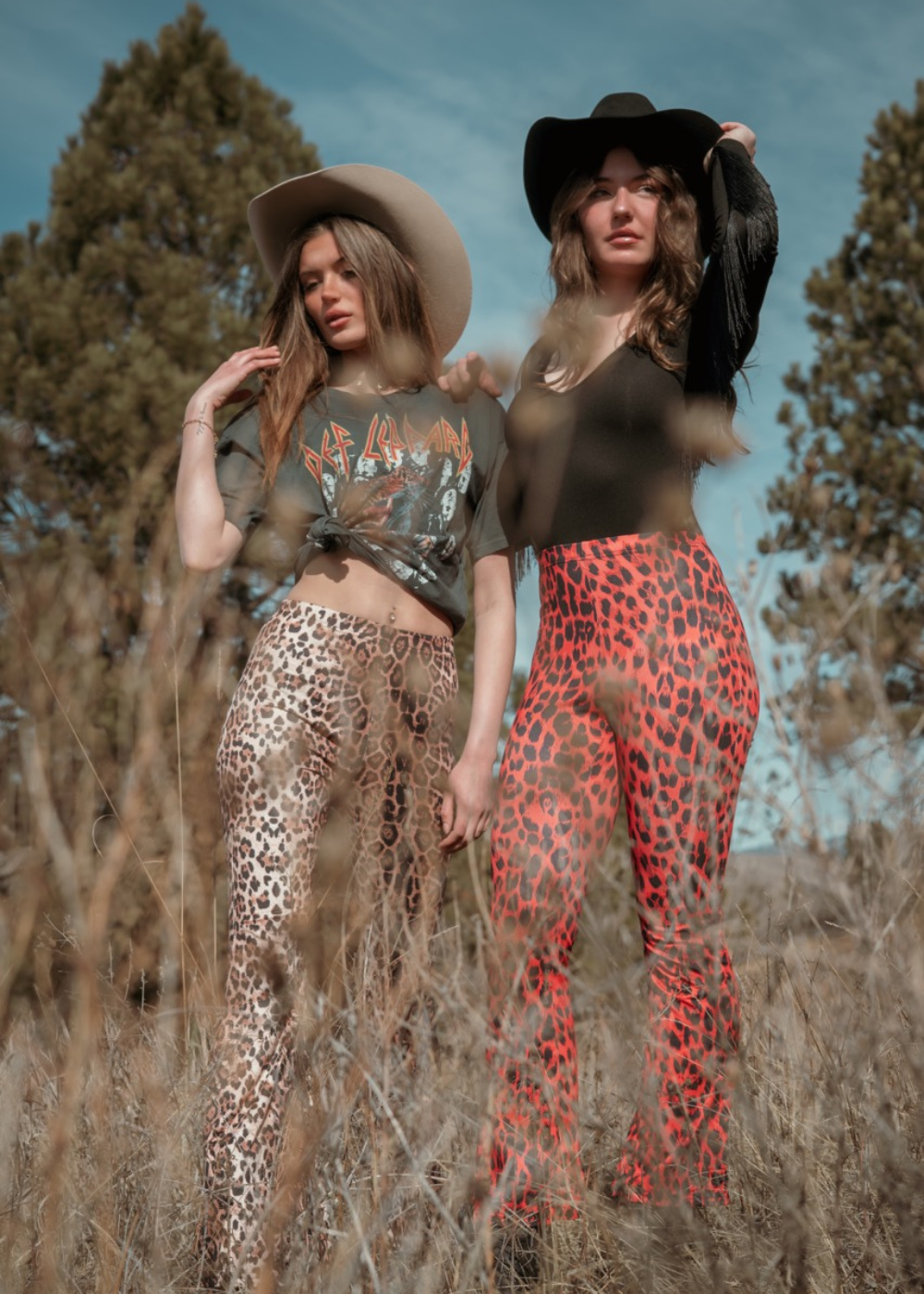 Two women standing in a field wearing leopard print pants and hats.