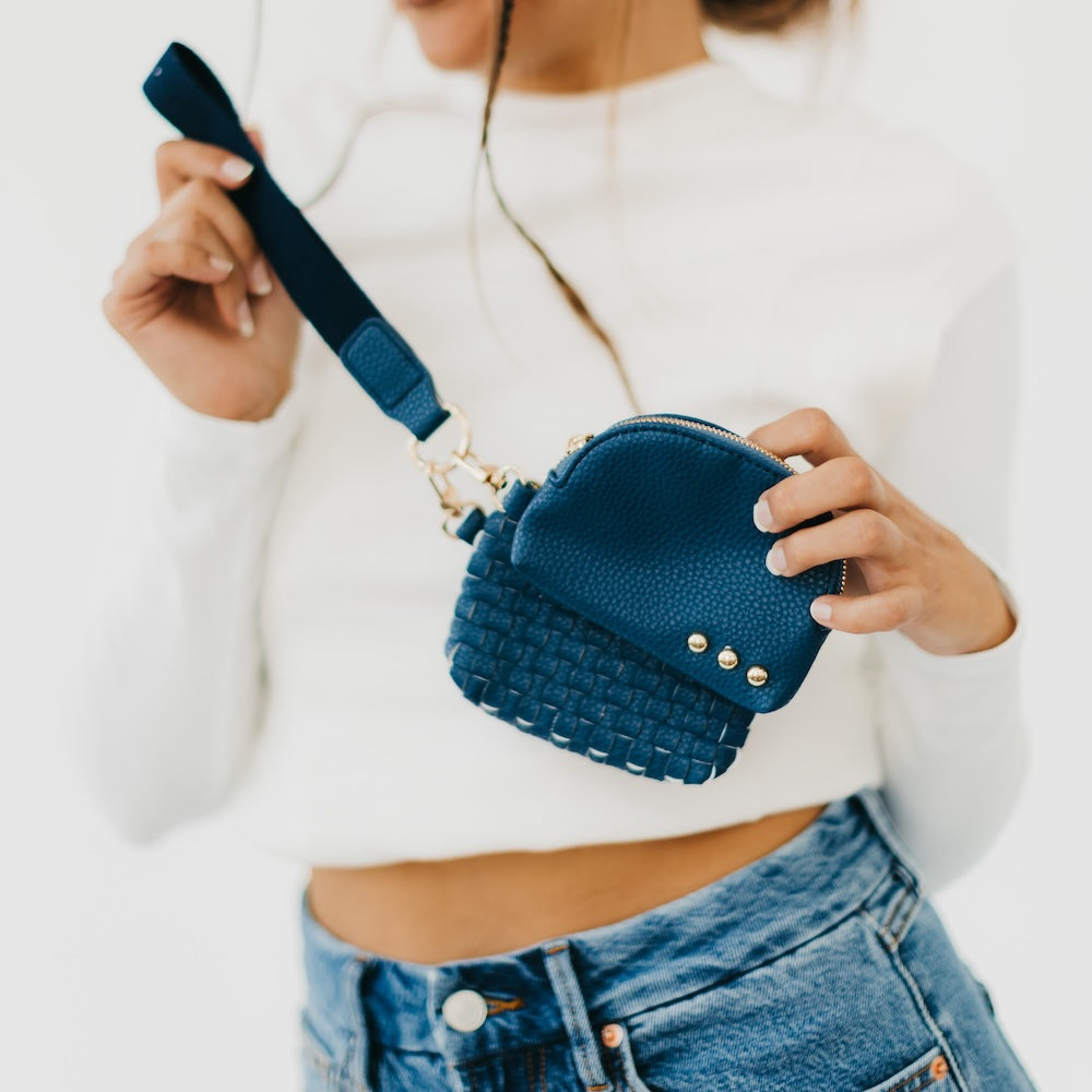 Person holding a blue woven handbag with a strap against a white background