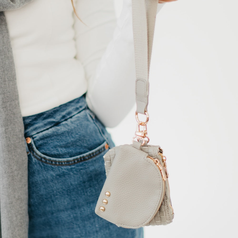 Small gray purse with gold accents held by a person wearing a gray cardigan and blue jeans.