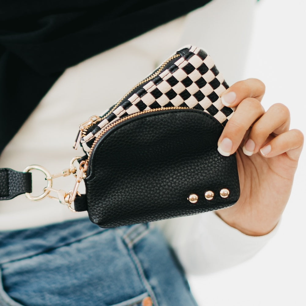 Black textured wallet with checkered flap held by a hand, wearing a white shirt and blue jeans.