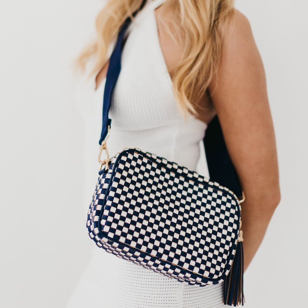 Woman wearing a navy and white checkered bag with a tassel on a light background