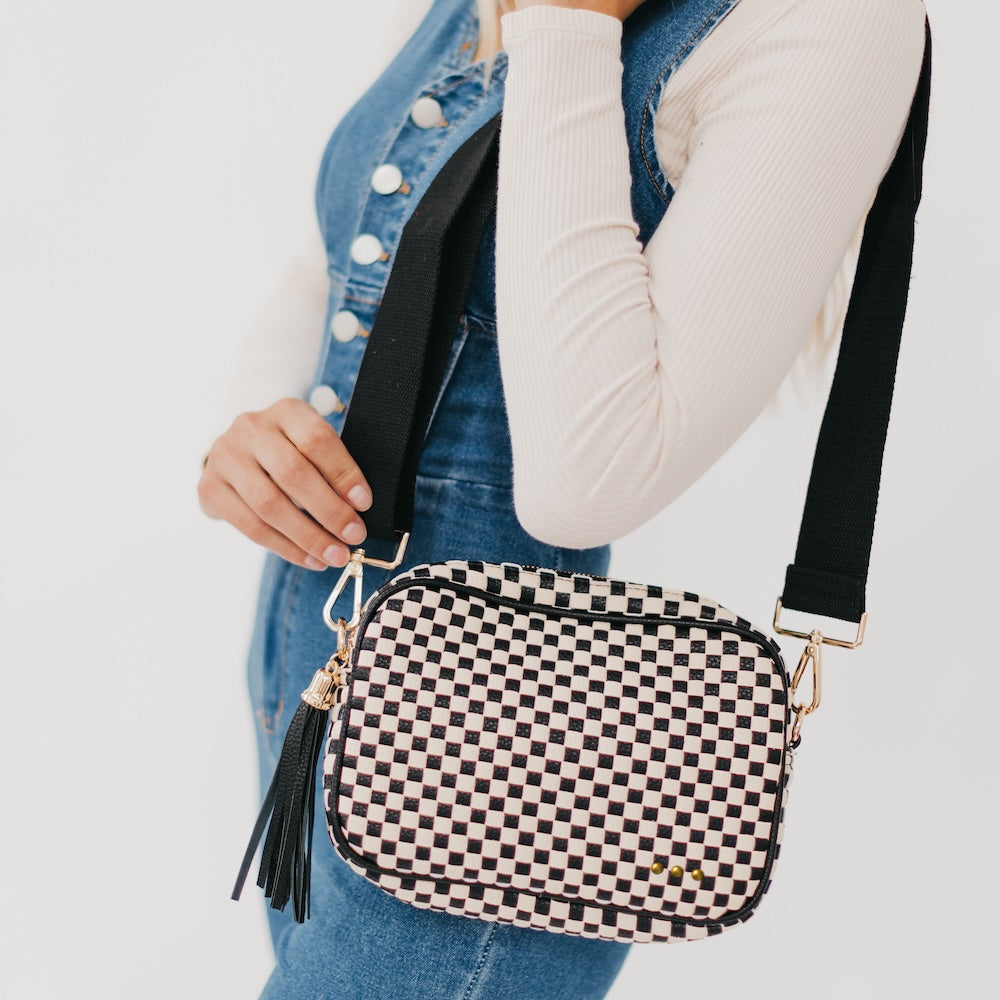 Person holding a black and white checkered handbag with a tassel on a light gray background