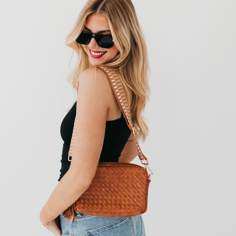 Woman wearing sunglasses and a brown textured handbag on a plain background