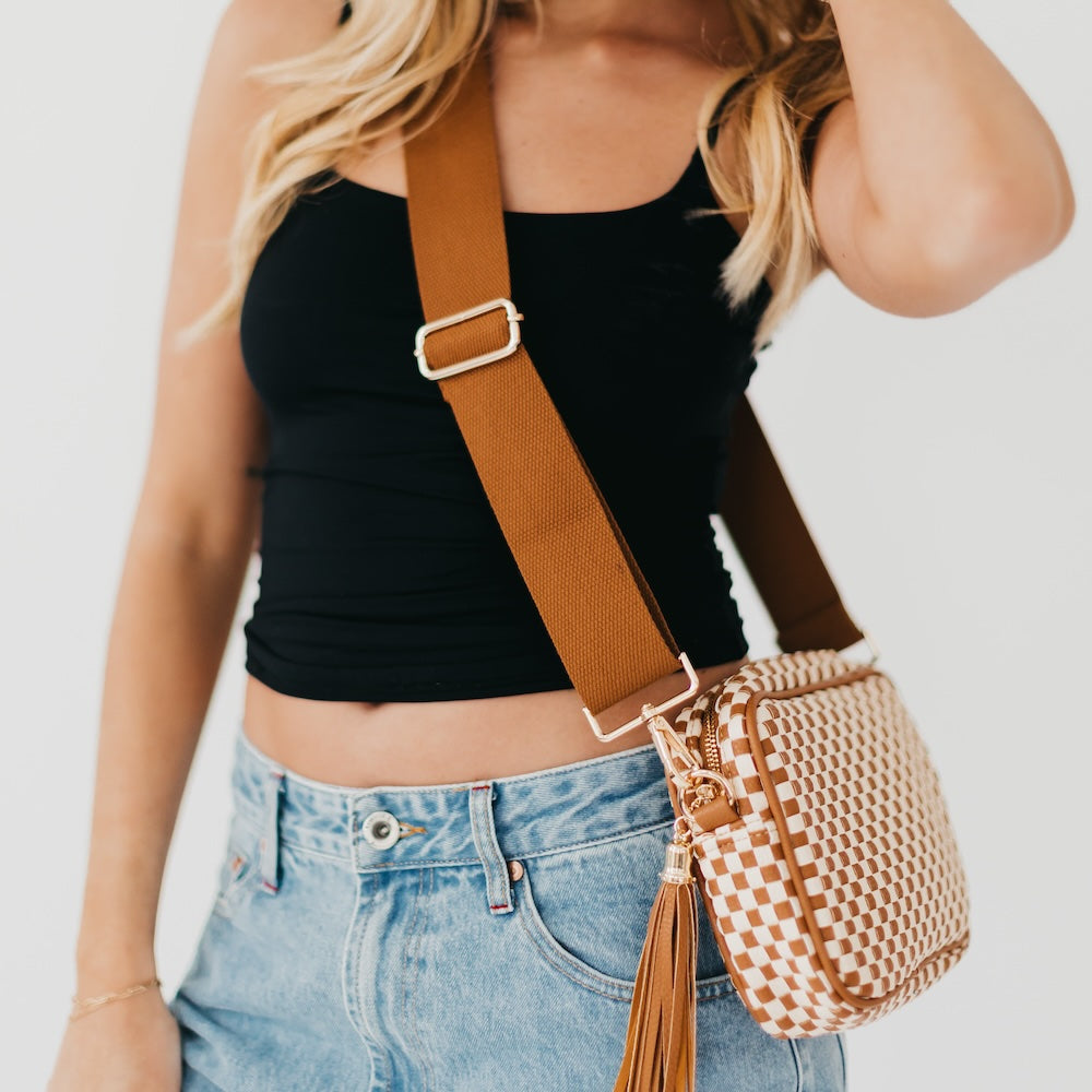 Woman wearing a black top and blue jeans with a brown crossbody bag on a white background