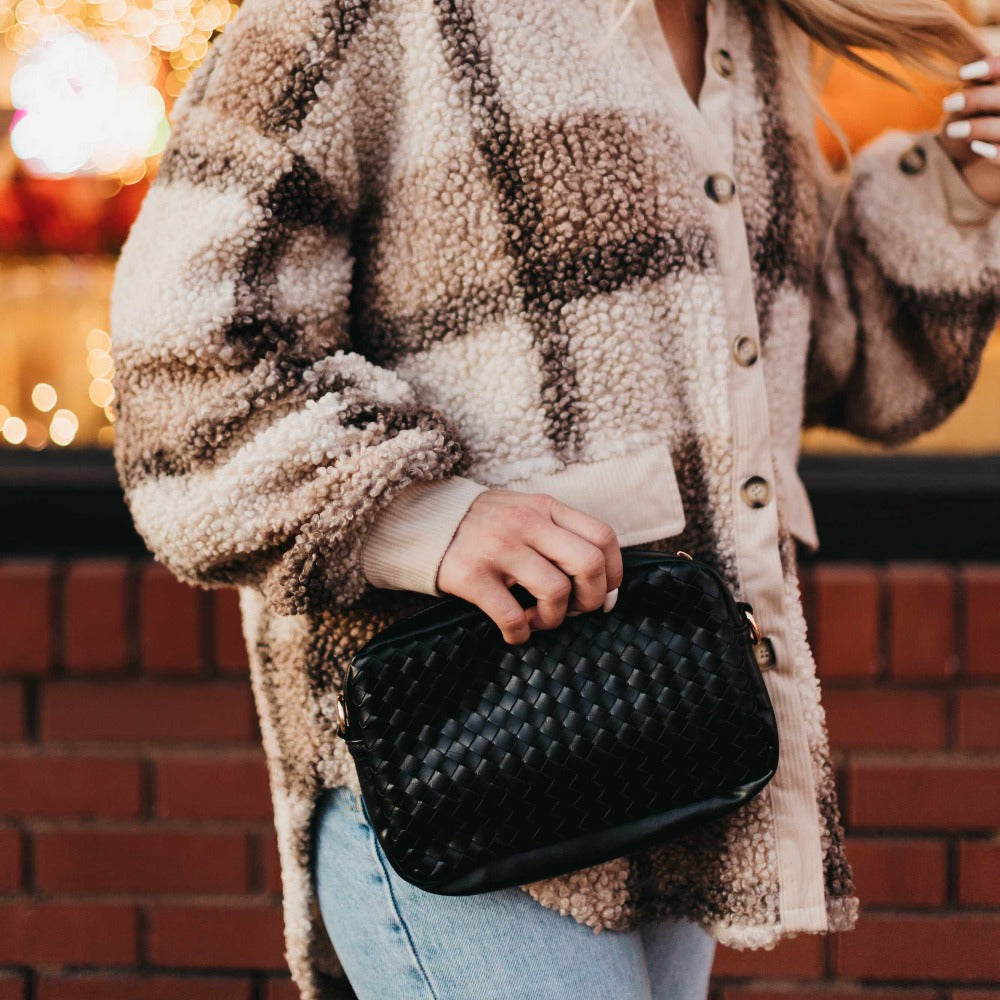 Person wearing a plaid coat holding a black handbag against a blurred background