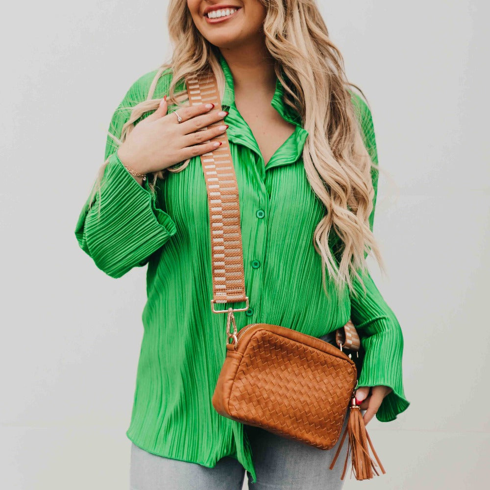 Woman wearing a green shirt holding a brown handbag against a plain background