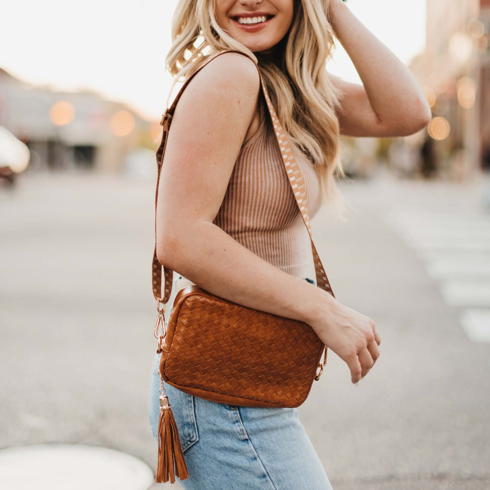 Woman holding a brown leather handbag with tassel on a blurred street background