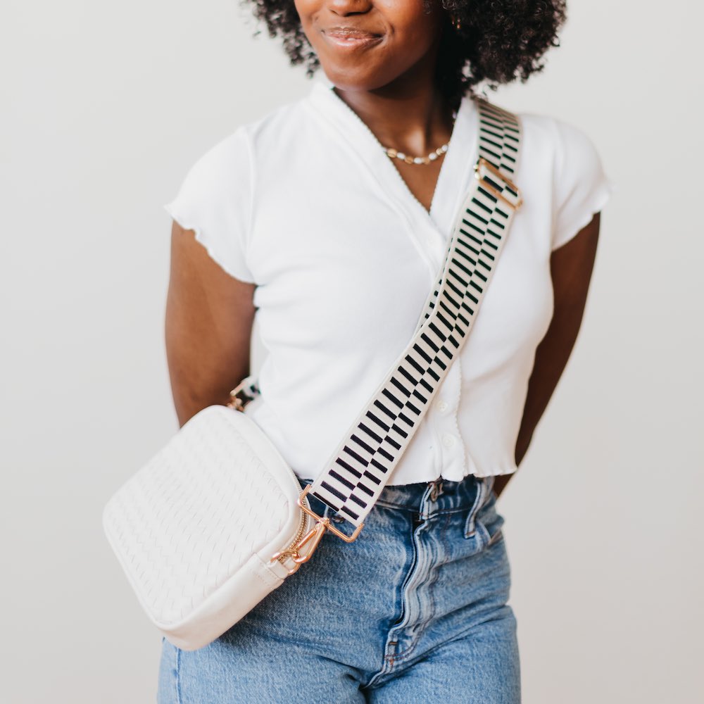 Woman wearing a white top, blue jeans, and a striped bag against a plain background