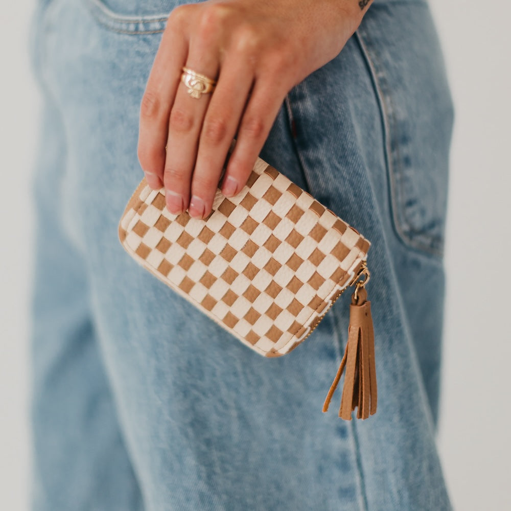 Hand holding a checkered wallet with a tassel against a blurred denim background